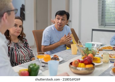 Diverse Family Meeting And Having Dinner Together Sitting At The Table At Home. Caucasian Couple Visiting Relatives. People Enjoy Talking While Eating Food.