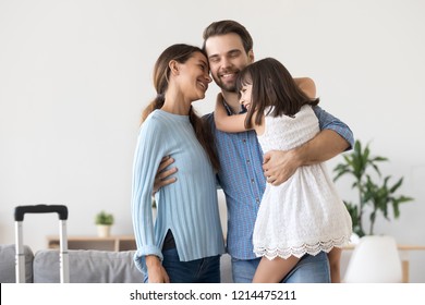 Diverse Family Standing Hugging In Living Room. Married Couple And Little Daughter Going On Vacation Suitcase Luggage Is Ready For Journey. Father Arrived After Long Business Trip. Reunion Concept