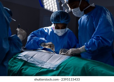Diverse female doctors with face masks doing surgery in hospital operating room. Medicine, healthcare and medical services, unaltered. - Shutterstock ID 2395115433