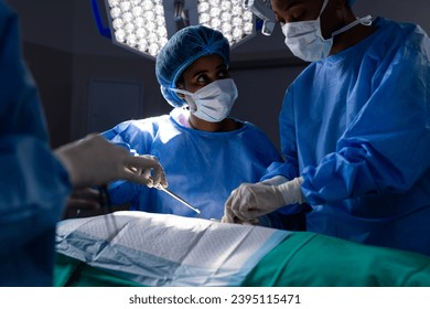Diverse female doctors with face masks doing surgery in hospital operating room. Medicine, healthcare and medical services, unaltered. - Shutterstock ID 2395115471