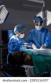 Diverse female doctors with face masks doing surgery in hospital operating room. Medicine, healthcare and medical services, unaltered. - Shutterstock ID 2395116197