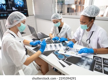 Diverse female doctors look at medical x-ray then diagnose and discuss before surgery at a hospital. Surgeon and radiologist teamwork talking, analysis x-ray film before treatment. Selective Focus. - Powered by Shutterstock