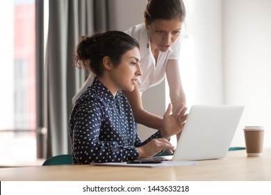 Diverse Female Mentor And Intern Talking Pointing On Laptop At Work Desk, Serious Caucasian Teacher Mentor Coach Teach Indian Trainee Looking At Computer In Office, Internship Apprentice Mentoring