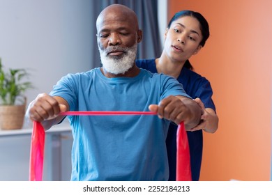 Diverse female physiotherapist helping senior male patient exercise with band, copy space. Hospital, medical and healthcare services. - Powered by Shutterstock