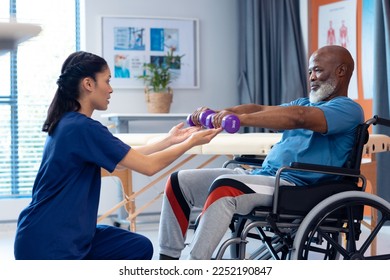 Diverse female physiotherapist helping senior male patient in wheelchair exercise with dumbbells. Hospital, medical and healthcare services. - Powered by Shutterstock