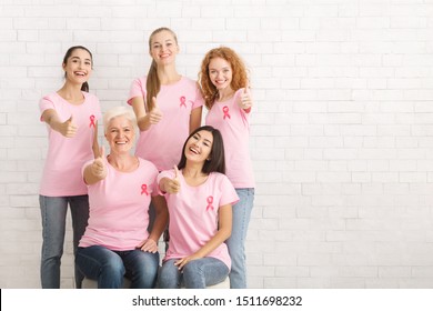 Diverse Female Volunteers In Pink Breast Cancer T-Shirts With Ribbons Gesturing Thumbs-Up Posing Over White Brick Wall. Copy Space - Shutterstock ID 1511698232