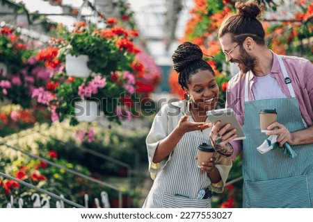 Diverse florist couple working at the plant nursery and drinking coffee while using tablet. Happy multiracial coworkers working in greenhouse and taking care of potted flowers. Copy space.