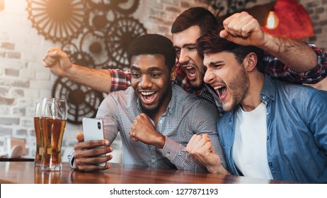 Diverse Football Fans Watching Football On Smartphone And Celebrating Victory Score In Pub