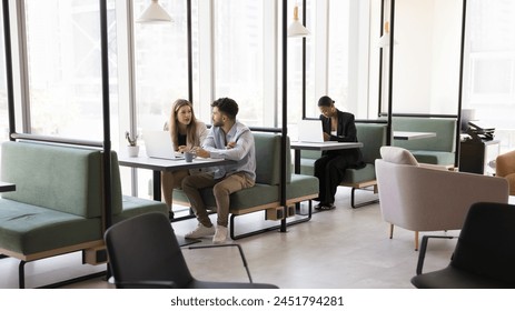 Diverse freelance project managers working at computers in modern coworking interior, sitting at tables, typing on laptops, talking, using online technology for business communication - Powered by Shutterstock