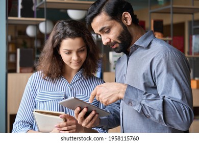 Diverse Friendly Coworkers Colleagues Indian Male Manager And Latin Female Employee Talking In Office Space Using Tablet Device. Effective Management, Teaching And Mentoring New Employee Concept.