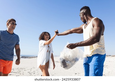 Diverse friends clean up a beach together, collecting trash. They show teamwork in an outdoor environmental conservation effort. - Powered by Shutterstock