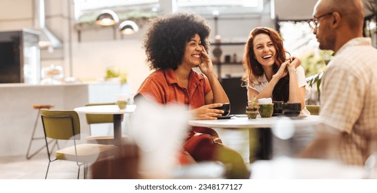 Diverse friends have a great time chatting in a trendy coffee shop, enjoying each other's company and making happy memories. Young people smiling happily on a social gathering. - Powered by Shutterstock