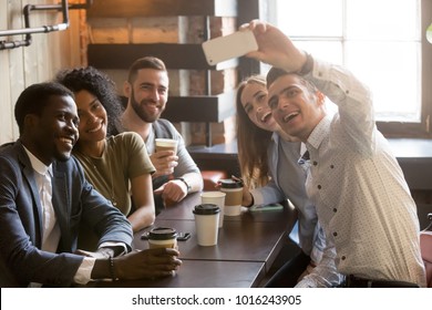 Diverse friends making selfie on smartphone together in cafe, young man holding phone shooting video or taking photo on mobile of african and caucasian millennial people sitting at coffee shop table - Powered by Shutterstock