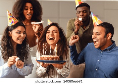 Diverse friends united in birthday celebration, lady celebrating with fellow students making a wish and enjoying bday party together at her home, sharing laughter and warmth of their friendship