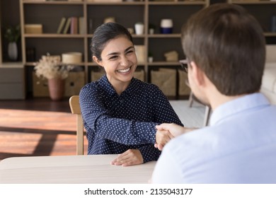 Diverse gender entrepreneurs business partners sit at desk handshake close deal satisfied with negotiations result. Young Indian woman successful job applicant being hired on place shake man hr hand