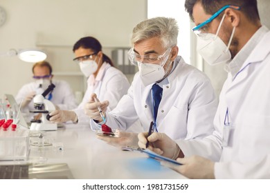 Diverse genetic scientists doing innovative food research in laboratory. Senior and young men and women in white coats, protective goggles and face masks develop GMO or fruit and vegetable pesticides - Powered by Shutterstock