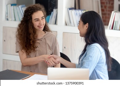 Diverse Girls Sitting At Table Shake Hands Greeting Each Other Begin Common Work Student Study Together, Asian Caucasian Interns New Company Employees Get Acquainted Or Starting Job Interview Concept