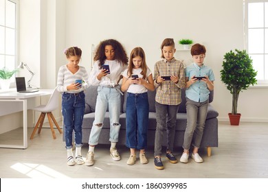 Diverse Group Of 8-10-year-old Children Playing Online Games On Smartphones. Kids, Immersed In Their Mobile Devices, Using Learning Apps, Chatting On Social Media, Blogging And Ignoring Real Life