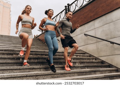 Diverse group of active smiling multiracial sportswomen and sportsman wearing sportwear run down the stairs training in city. Movement, motivation, sport concept