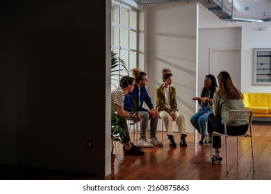 A Diverse Group Of Adults Sit In A Circle In Their Chairs And Listen To And Sympathize With Each Other With Serious Expressions.