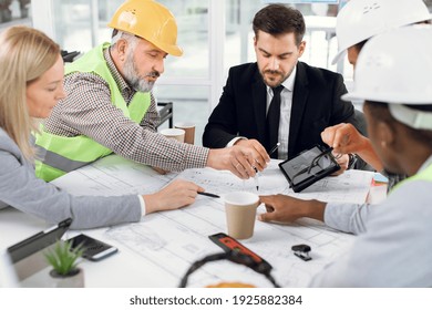 Diverse Group Of Architects, Designers And Engineers Sitting At Table With Modern Gadgets And Blueprints. Business People Working On Common Building Project.