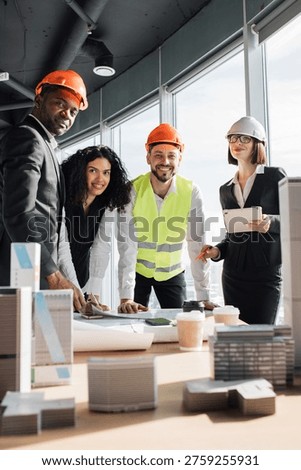 Diverse group of architects and engineers collaborating on a building project with blueprints and models on a table