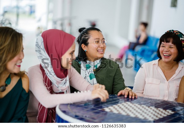 A diverse group of Asian women friends sit around a\
table to talk, gossip and chat. They are from multiple ethnicities\
and are smiling and laughing as they converse in a relaxed, easy\
and light way.
