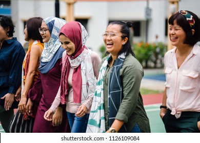 A diverse group of Asian women (Malay and Chinese) walk side by side in a basketball court and are laughing as they walk. 