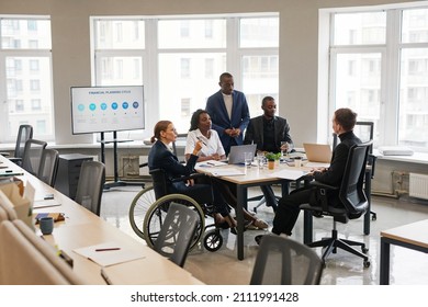 Diverse Group Of Business People At Meeting Table In Office With Woman Using Wheelchair In Leadership