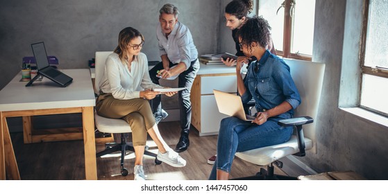 Diverse group of business people working together at a small office. Woman showing her digital tablet and discussing new business plan with coworkers.