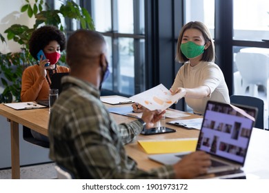 Diverse group of business people working in creative office. group of people wearing face masks and giving documents. social distancing protection hygiene in workplace during covid 19 pandemic.