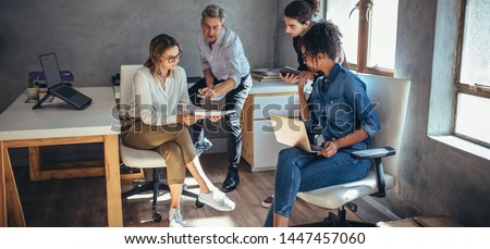 Diverse group of business people working together at a small office. Woman showing her digital tablet and discussing new business plan with coworkers.