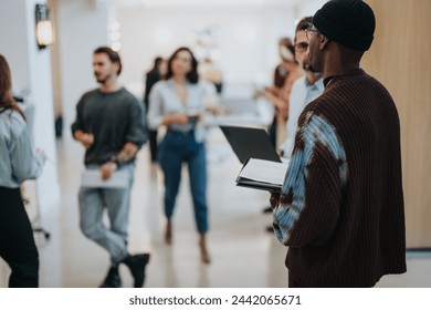 Diverse group of businesspeople in informal attire conversing and walking in an office corridor, depicting a relaxed workplace culture. - Powered by Shutterstock