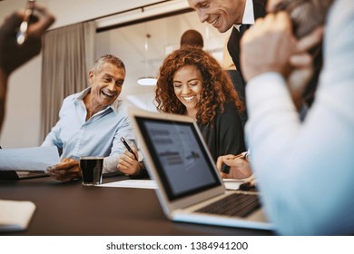 Diverse group of businesspeople laughing together while having a meeting around a table in an office boardroom