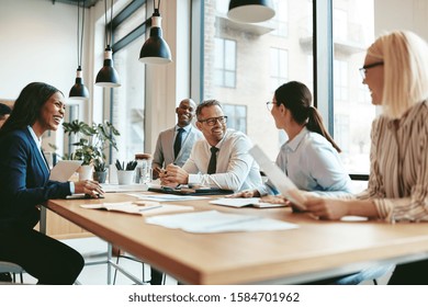 Diverse group of businesspeople laughing while discussing paperwork together during a meeting around a table in a modern office - Shutterstock ID 1584701962