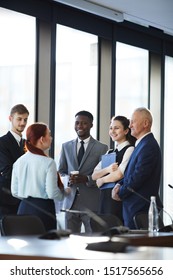 Diverse Group Of Cheerful Business People Talking Actively While Standing By Window In Conference Room