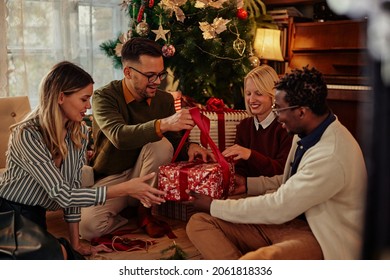 Diverse group of cheerful friends sitting on the floor by Christmas tree and opening gifts together - Powered by Shutterstock