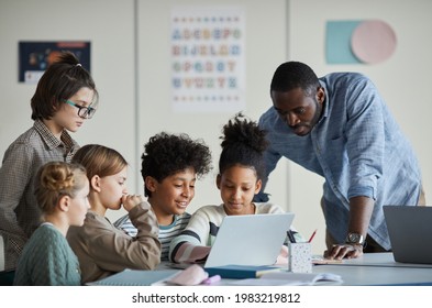 Unterschiedliche Gruppen von Kindern mit männlichem Lehrer, die gemeinsam in der modernen Schulklasse Laptop benutzen