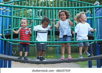 A Diverse Group Of Children Are Playing Together On The Playground Equipment. The Kids Are Of Difference Races, Including African American, Hispanic And White. The Happy Children Are Jumping 