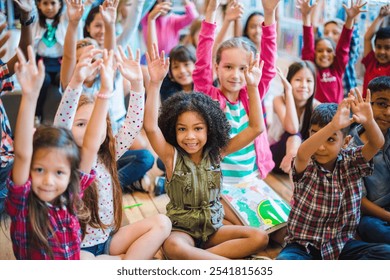 Diverse group of children sitting on the floor, smiling and raising hands. Happy kids in a classroom setting, showing enthusiasm and engagement. Cute little diverse kids smiling at camera. - Powered by Shutterstock