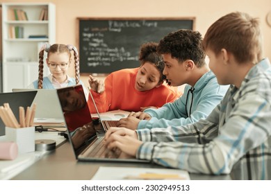 Diverse group of children using laptops in school classroom with black girl peeking at computer screen - Powered by Shutterstock