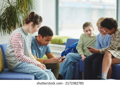 Diverse Group Of Children Using Smartphones In School During Break All Dressed In Colorful Clothes