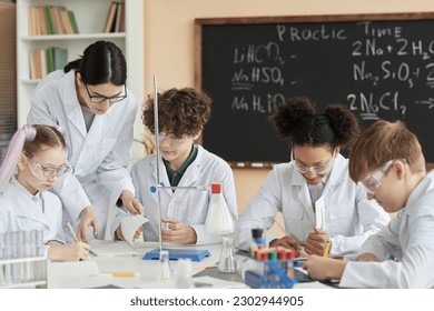 Diverse group of children wearing lab coats in science class at school with teacher helping - Powered by Shutterstock