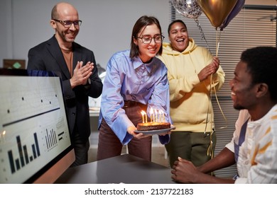 Diverse group of colleagues applauding while bringing surprise Birthday cake to smiling young man in office - Powered by Shutterstock