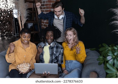 Diverse group of college students, friends, young people watching football or baseball game on laptop, have fun, eating popcorn. Concept of international friendship, leisure time, home activity - Powered by Shutterstock