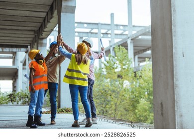 A diverse group of construction workers in safety gear celebrate a successful project with a team high five at a building site. - Powered by Shutterstock