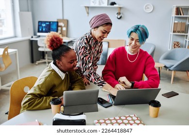 Diverse group of creative young people using laptop during meeting in office and smiling cheerfully Stock Photo