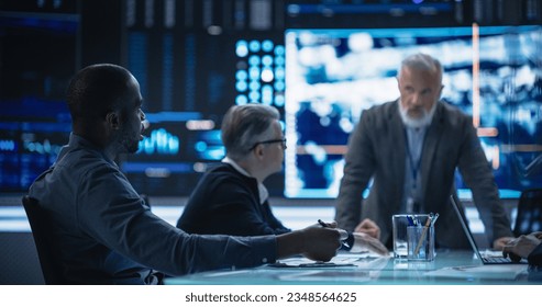 Diverse Group of Cybersecurity Experts Monitoring an Active Operation with Satellite Tracking Technology. Black Male Specialist Pitching an Idea for Tracking a Target Vehicle in Urban Terrain - Powered by Shutterstock