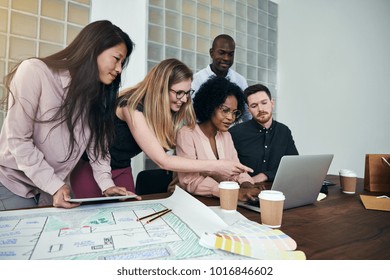 Diverse group of designers smiling and talking while working together over a laptop at a desk in a modern office