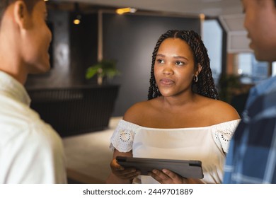 Diverse group discussing in a modern business office, biracial woman holding tablet. She has brown eyes, braided hair, wearing off-shoulder top; men in casual shirts, unaltered - Powered by Shutterstock